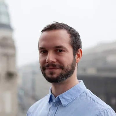 Daniel Müller lächelt auf einer Dachterrasse in Berlin, mit unscharfem Hintergrund und modernem Look.